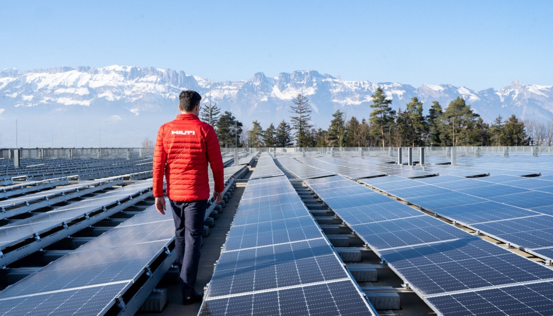 Man walking on roof next to solar panels in a mountain region.