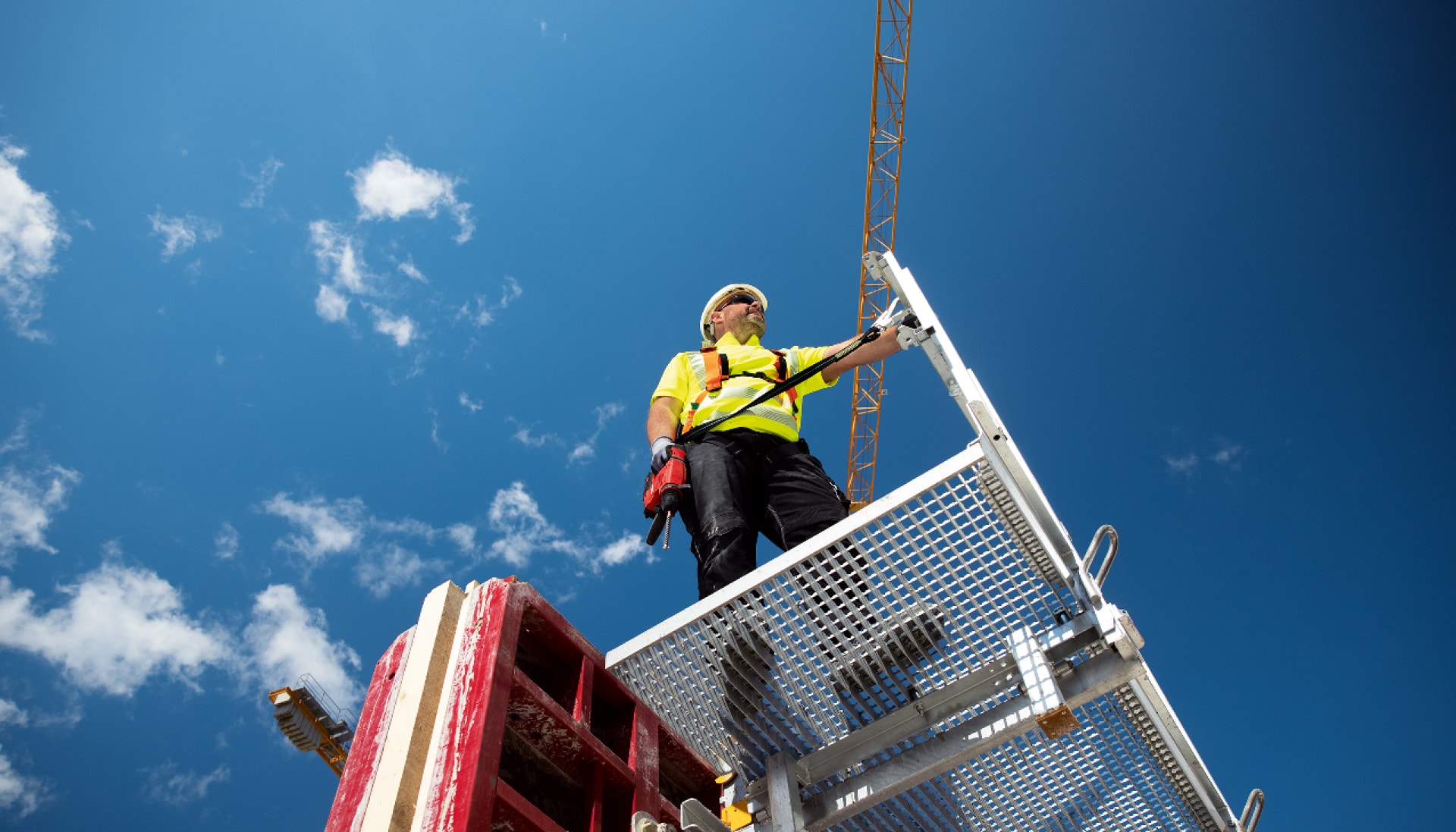 Worker standing on a platform with a drill in his hand that is fixed to a pole with a tool tether